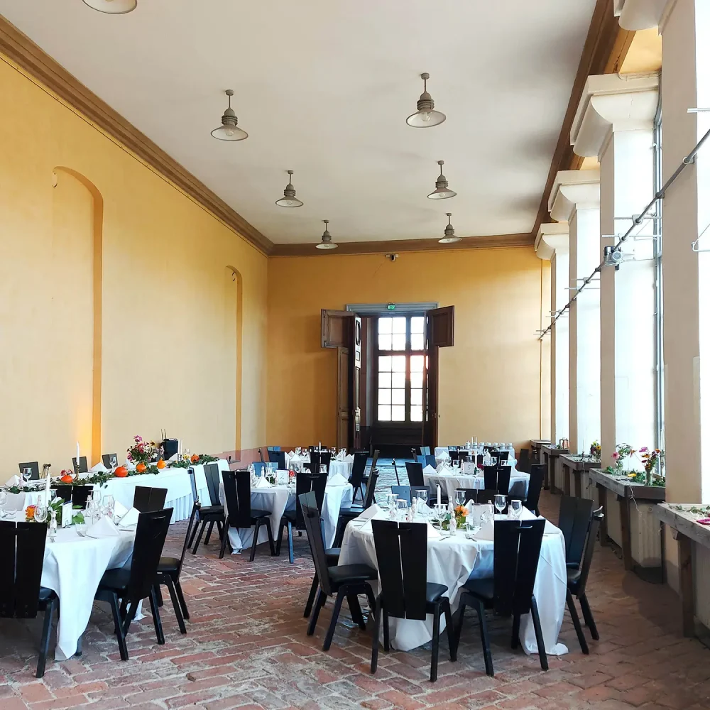 Dukade bord för festmiddag i Orangeriet i Botaniska trädgården i Uppsala, med vita dukar, blomsterdekorationer och historisk miljö.