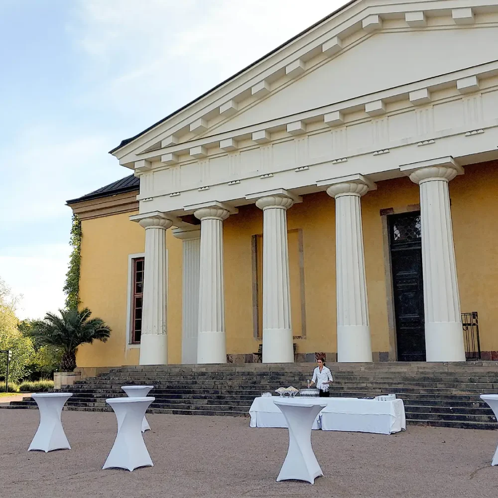 Festdukning utanför Orangeriet i Botaniska trädgården i Uppsala, med ståbord och serveringsbord framför den klassiska byggnaden med pelare.